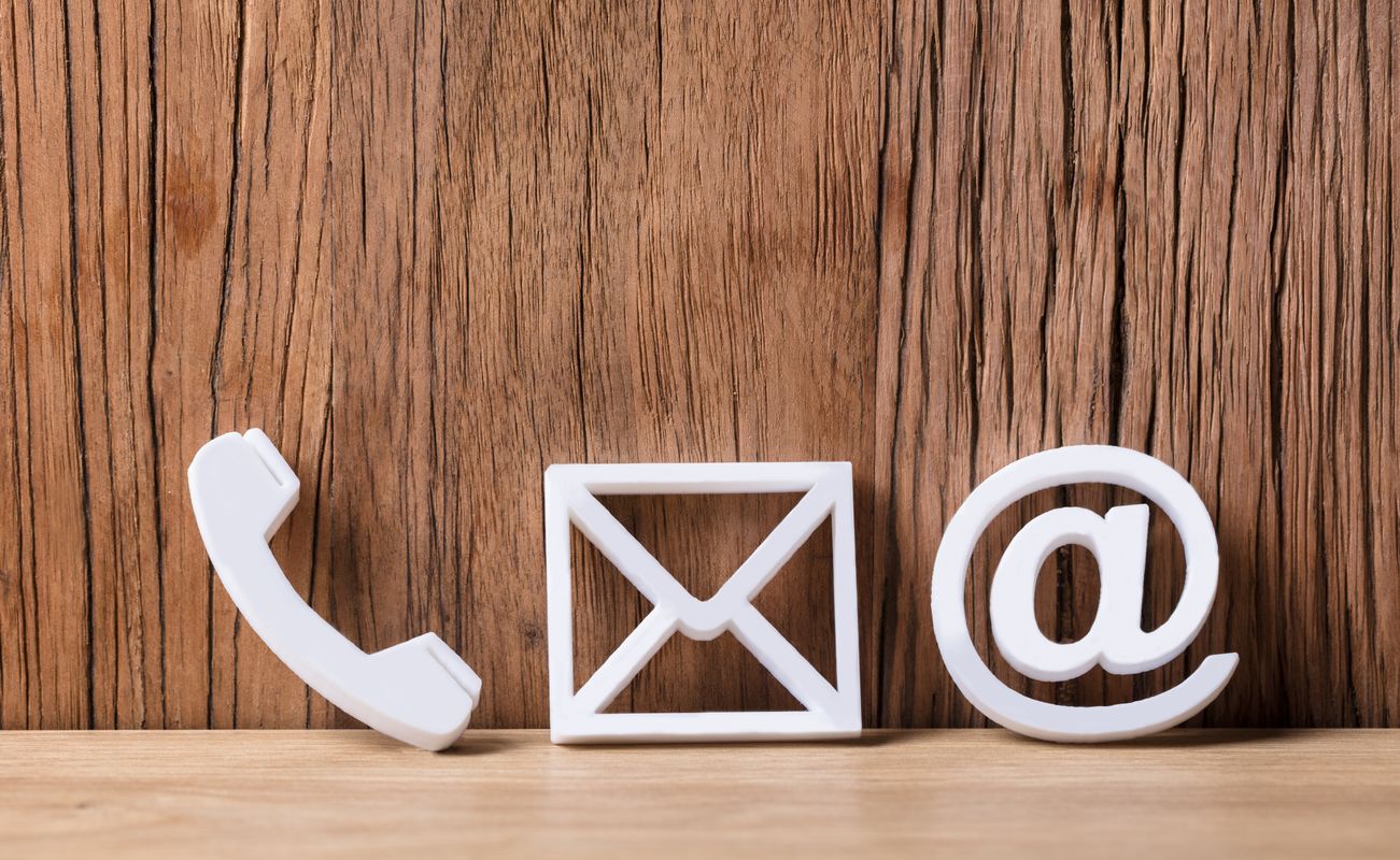 Weiße Symbole für Telefon, E-Mail und @-Zeichen vor einer Holzoberfläche.